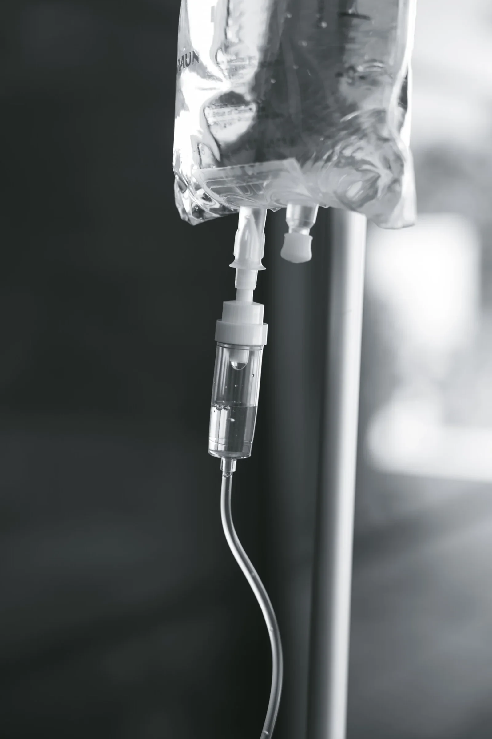 Close-up of a hanging IV bag and drip chamber, the line curving away out of frame