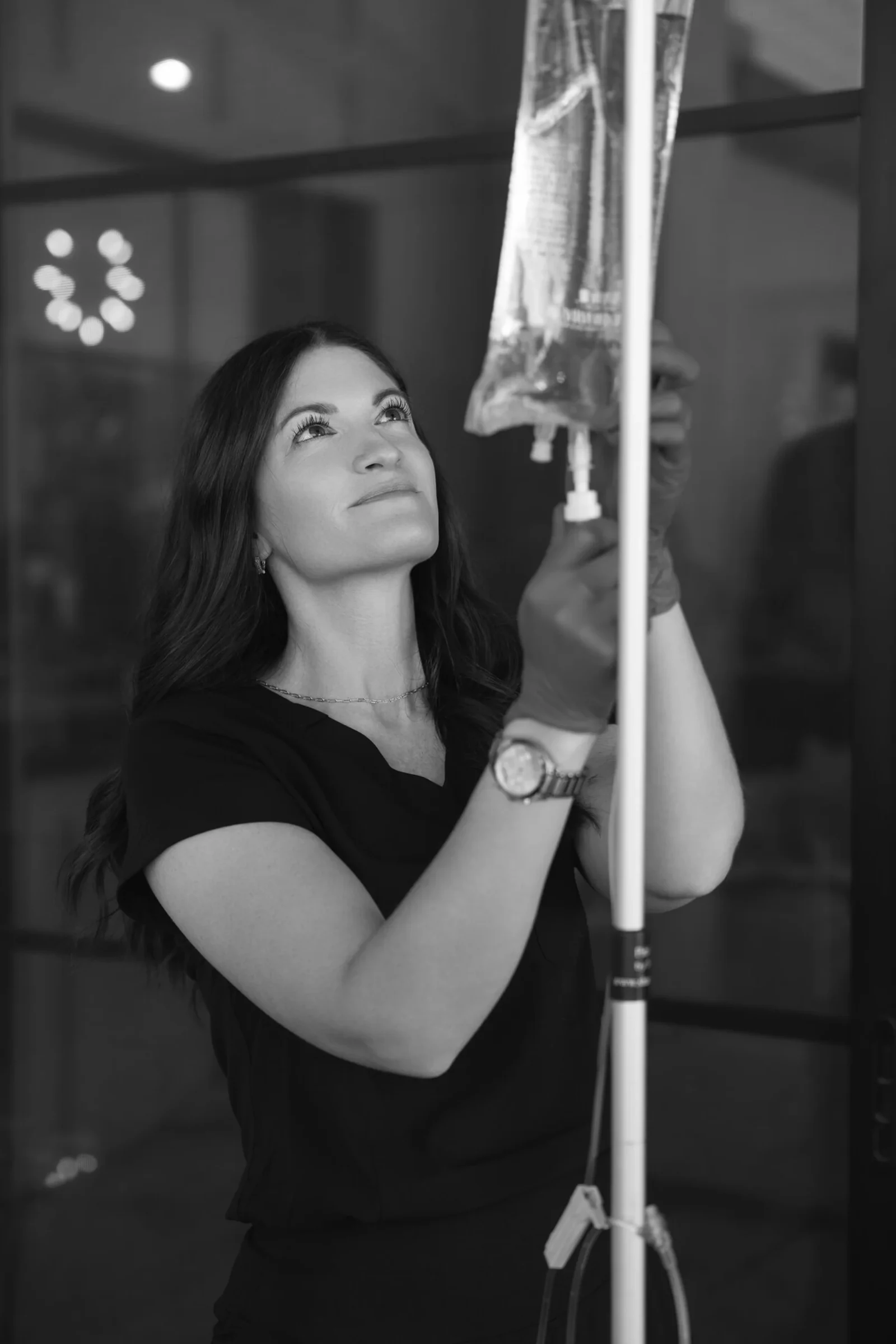A registered nurse looking up as she checks the drip rate on the stand, in black and white