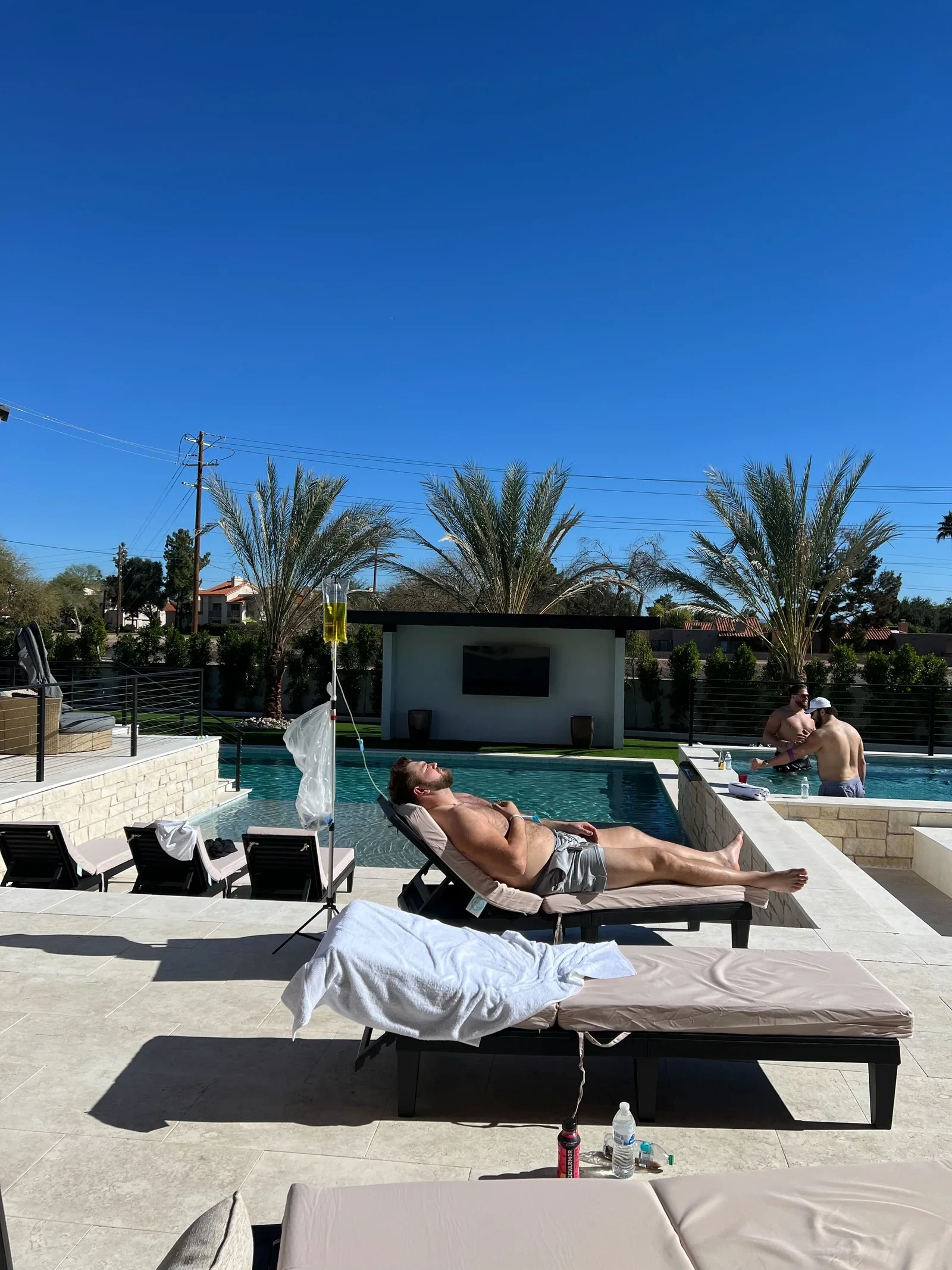 A client on a poolside lounger under a clear Arizona sky, receiving an IV with palm trees behind