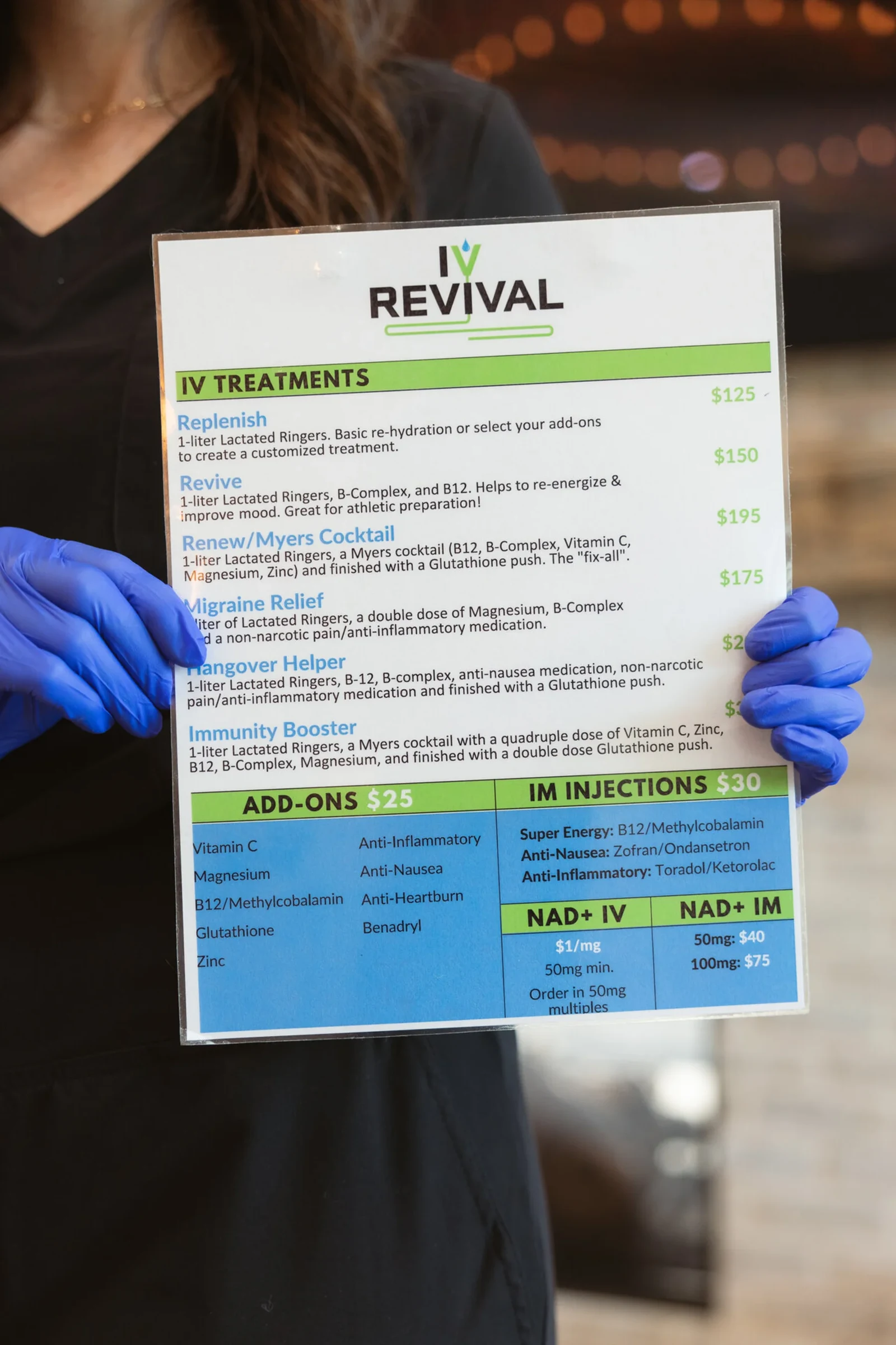 A nurse in gloves holding up the IV Revival treatment menu, the drips and add-ons listed on it