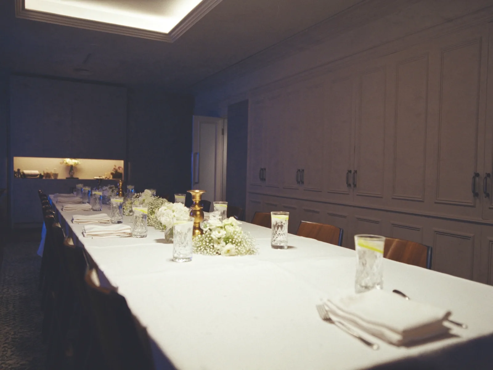 A private dining room set for a celebration: a long linen table, cut glass, white flowers and brass candle holders