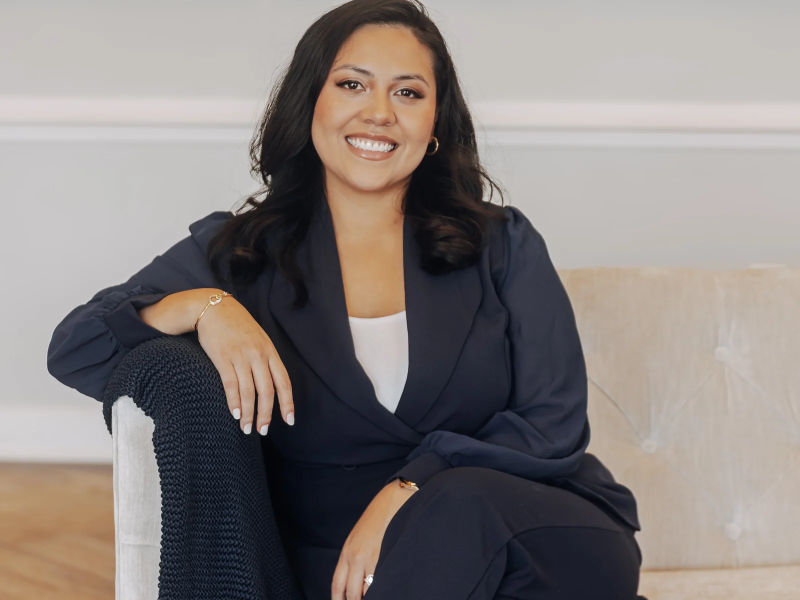 The founder of Top Tier Wellness, a board-certified physician assistant, seated in a navy suit on a cream sofa