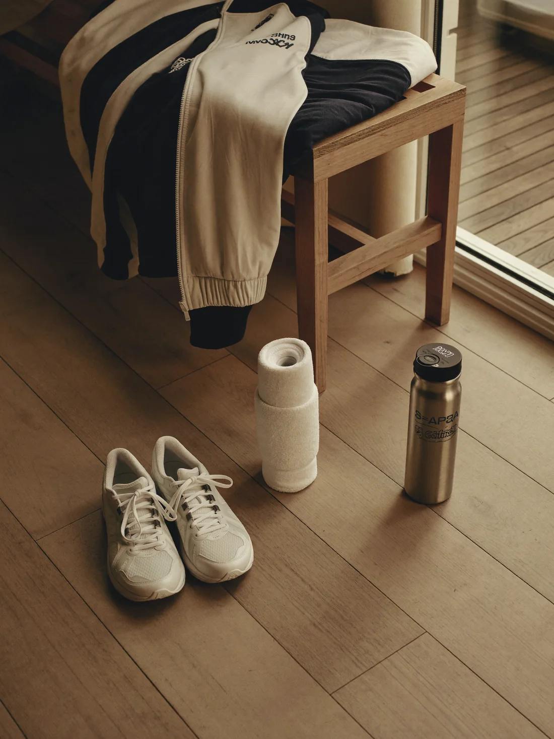 Running shoes, a water bottle and a folded jacket on pale oak floorboards in morning light