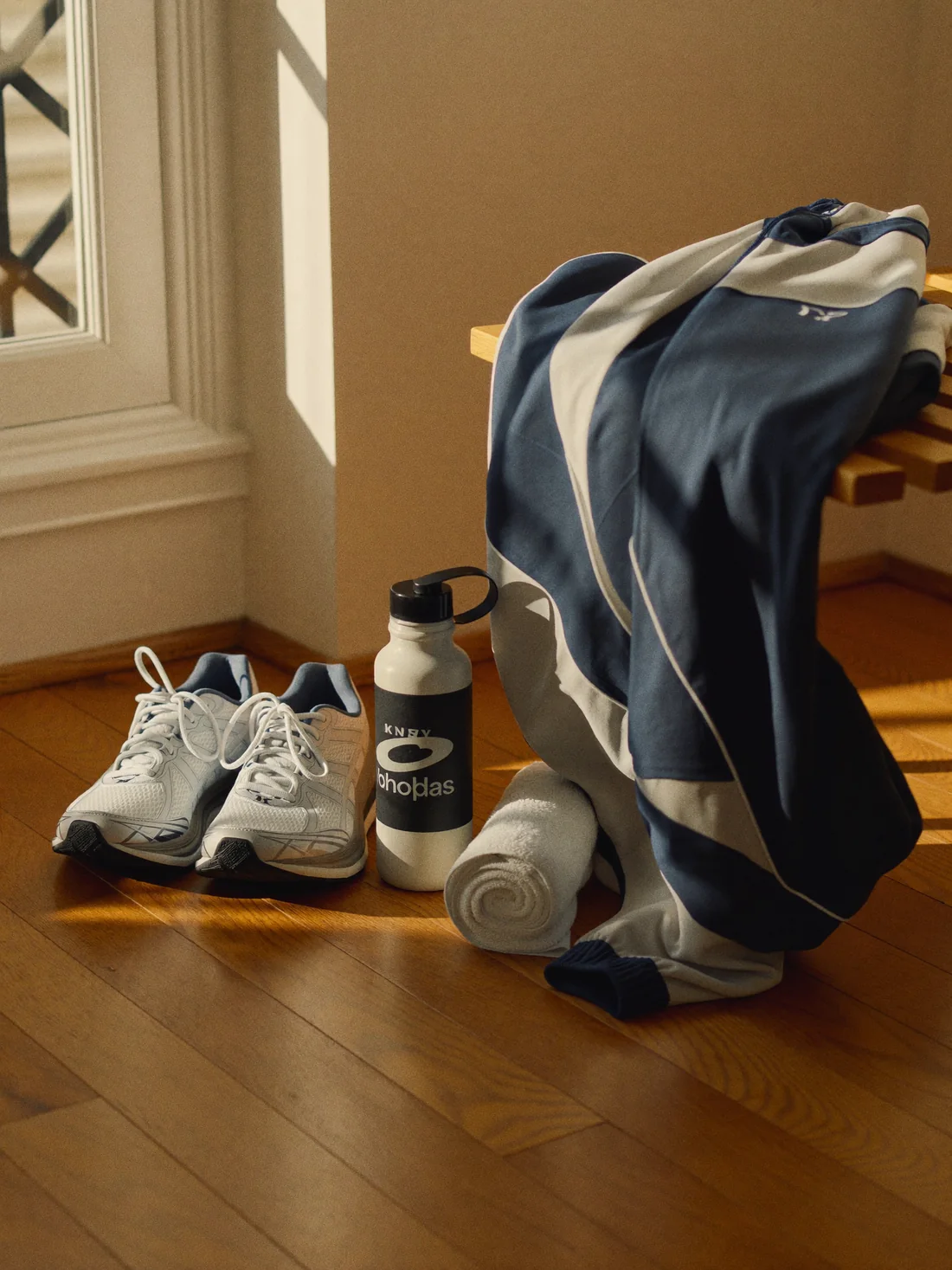 Running shoes, a water bottle and a folded jacket on pale oak floorboards in morning light