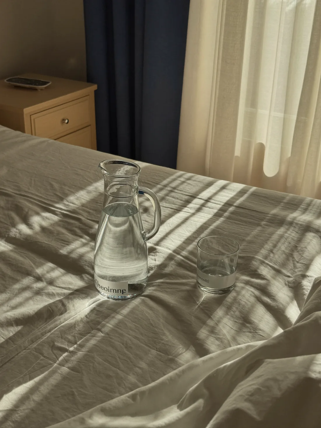 Morning sun across rumpled linen bedding with a glass carafe of water on the nightstand